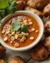 Finished homemade satay sauce served with grilled chicken skewers and garnished with peanuts and cilantro.