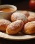 Beignets aux pommes moelleux présentés sur une assiette, avec un bol de sauce caramel, la délicieuse présentation des beignet au pomme.