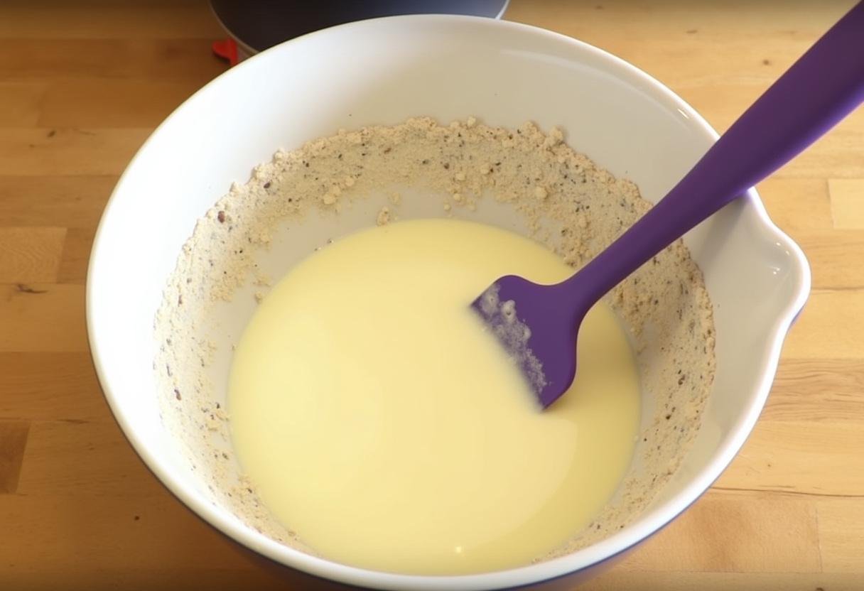 Incorporation des blancs d'œufs dans la préparation pour le financier moelleux aux amandes, utilisant une spatule en silicone sur une table en bois.