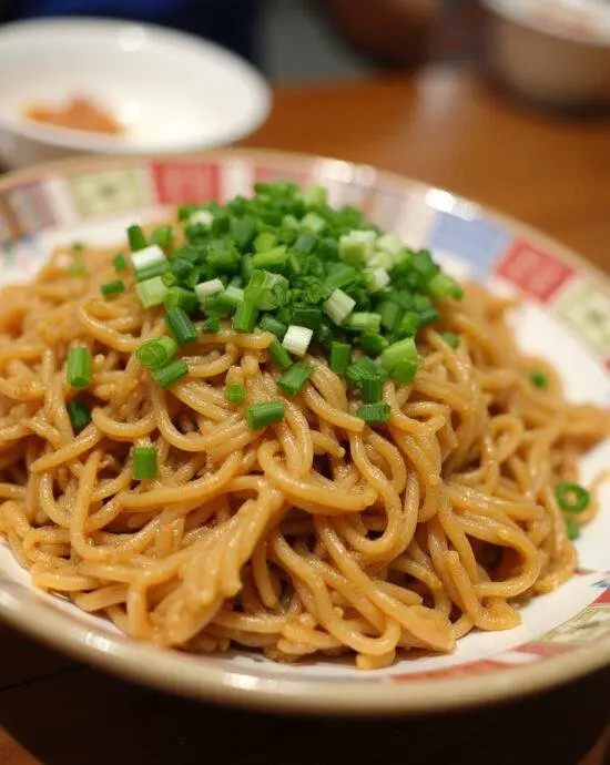 Nouilles sautées au poulet servies dans un bol, garnies d'oignons verts et de graines de sésame.