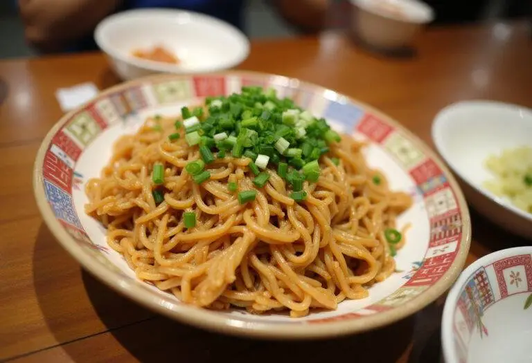 Nouilles sautées au poulet servies dans un bol, garnies d'oignons verts et de graines de sésame.