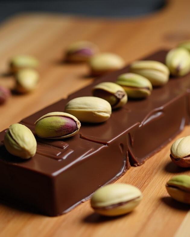 Tablette chocolat pistache croquante finie, décorée de pistaches sur un plateau en bois.