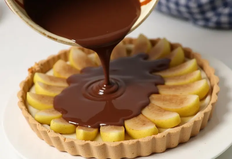 Versement de la ganache au chocolat sur la tarte au poire et au chocolat, pour un délice chocolaté.